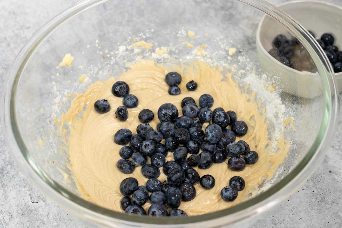 Muffin batter and blueberries in a glass bowl