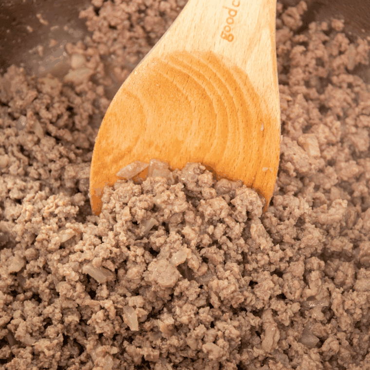 Ground beef browning in the Instant Pot, being stirred with a spoon.