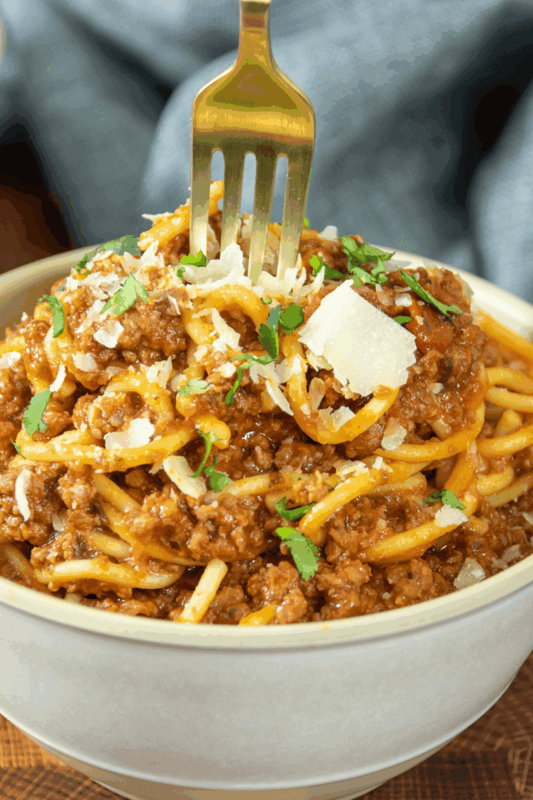 Bowl of Old Spaghetti Factory-style meat sauce served over spaghetti noodles, garnished with fresh herbs.