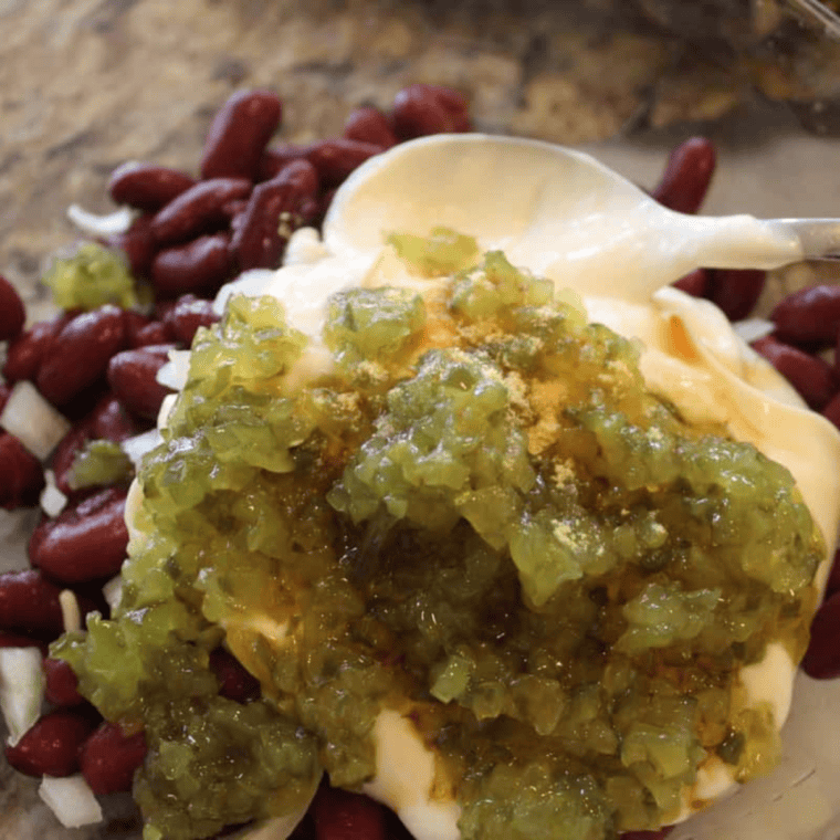 A mixing bowl with creamy ingredients like mayo, pickle relish, Worcestershire sauce, and horseradish being folded together.