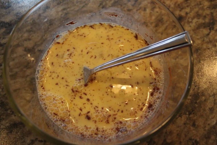 overhead process shot: beaten eggs, milk, vanilla, and cinnamon in a bowl with a fork to air fry french toast