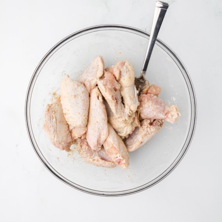 Raw chicken wings in a mixing bowl being coated with a Chinese-style seasoning.