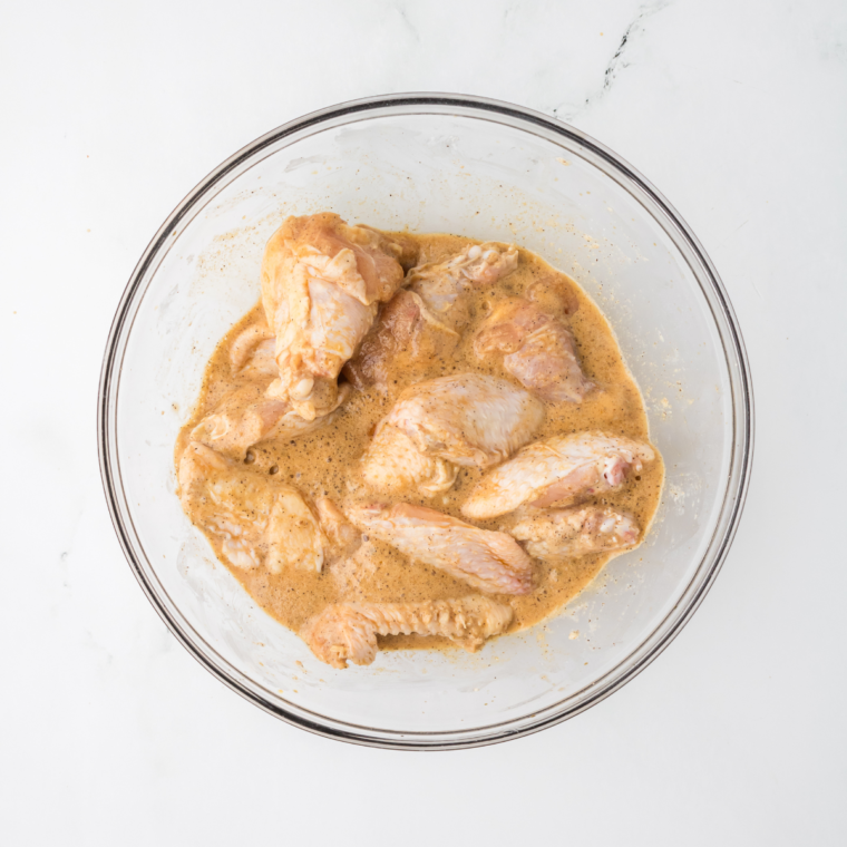 Raw chicken wings in a mixing bowl being coated with a Chinese-style marinade.