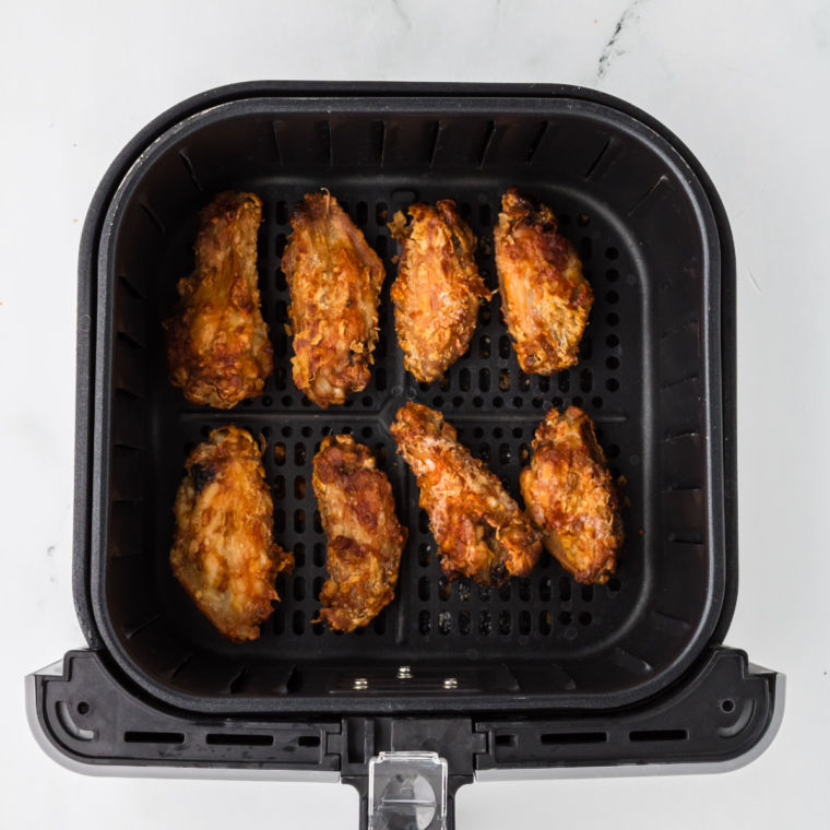 Golden, crispy chicken wings halfway through air frying, shown in the air fryer basket.