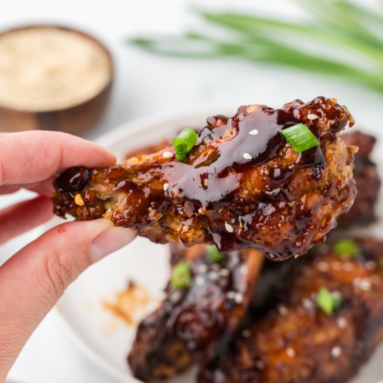 Air fryer Chinese chicken wings arranged on a plate, sprinkled with sesame seeds and sliced scallions.