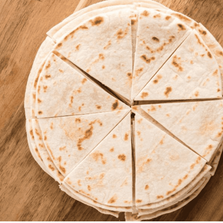 Cutting tortillas into triangles on a cutting board with a knife, preparing for air frying with melted butter ready to brush.