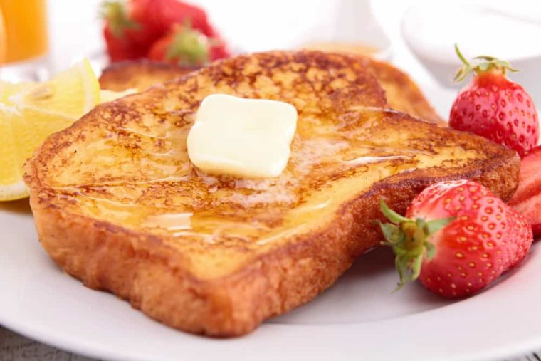 closeup: a piece of air fryer French toast on a plate with butter and maple syrup on top and strawberries to the side