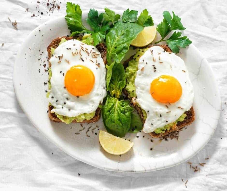 overhead: two air fryer fried eggs over avocado toast on a white plate with fresh herbs