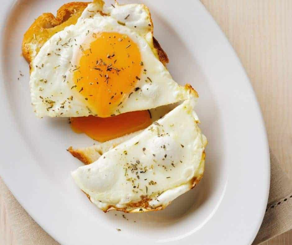 overhead: air fryer fried egg with a runny yolk on a piece of toast on a white plate