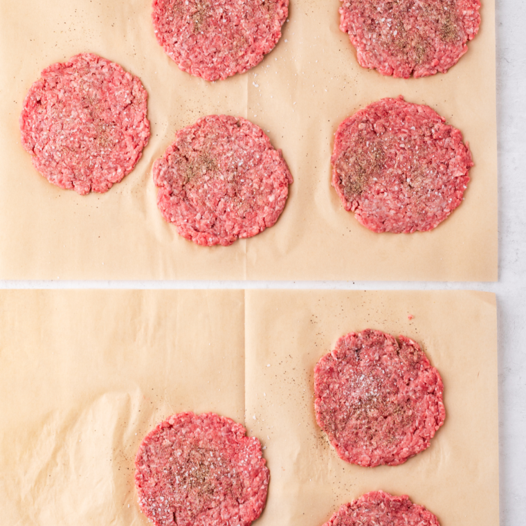 Eight evenly portioned and seasoned ground beef patties, each approximately 2 ounces, arranged on a cutting board.