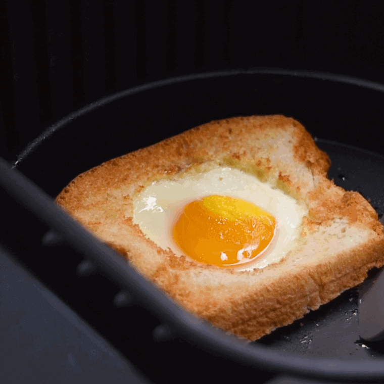 Toasted slice of bread with a fried egg cooked in the center, served Cracker Barrel-style on a plate with breakfast sides.