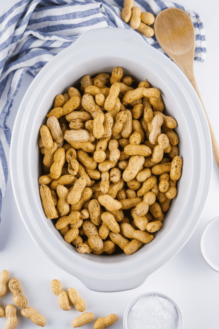 Season Generously: Cajun seasoning and spices sprinkled over peanuts in crockpot.