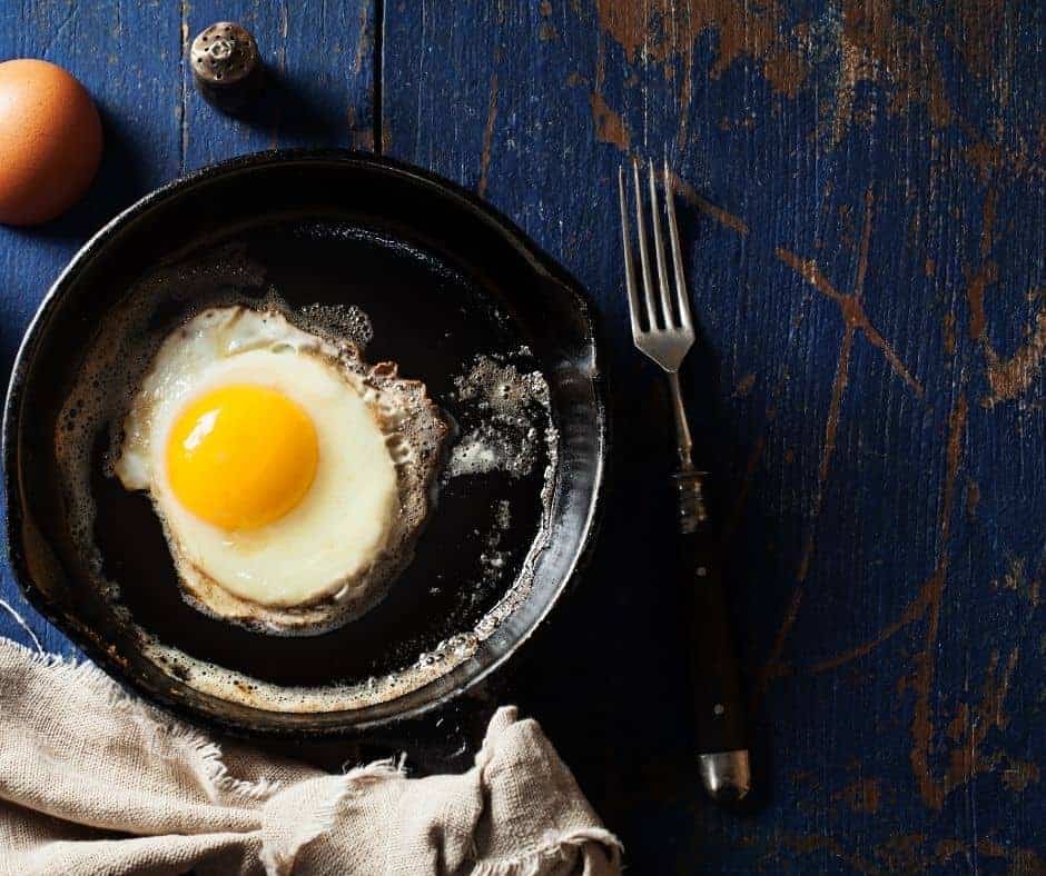 overhead: fried egg in air fryer safe skillet on a blue wooden table with a fork to the side