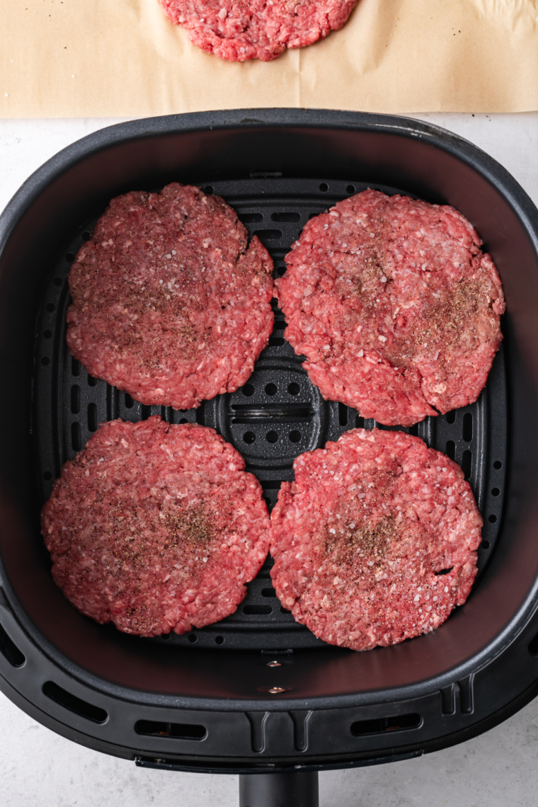 Seasoned beef patties arranged in a single layer in an air fryer basket, ready to be cooked at 375°F (190°C).