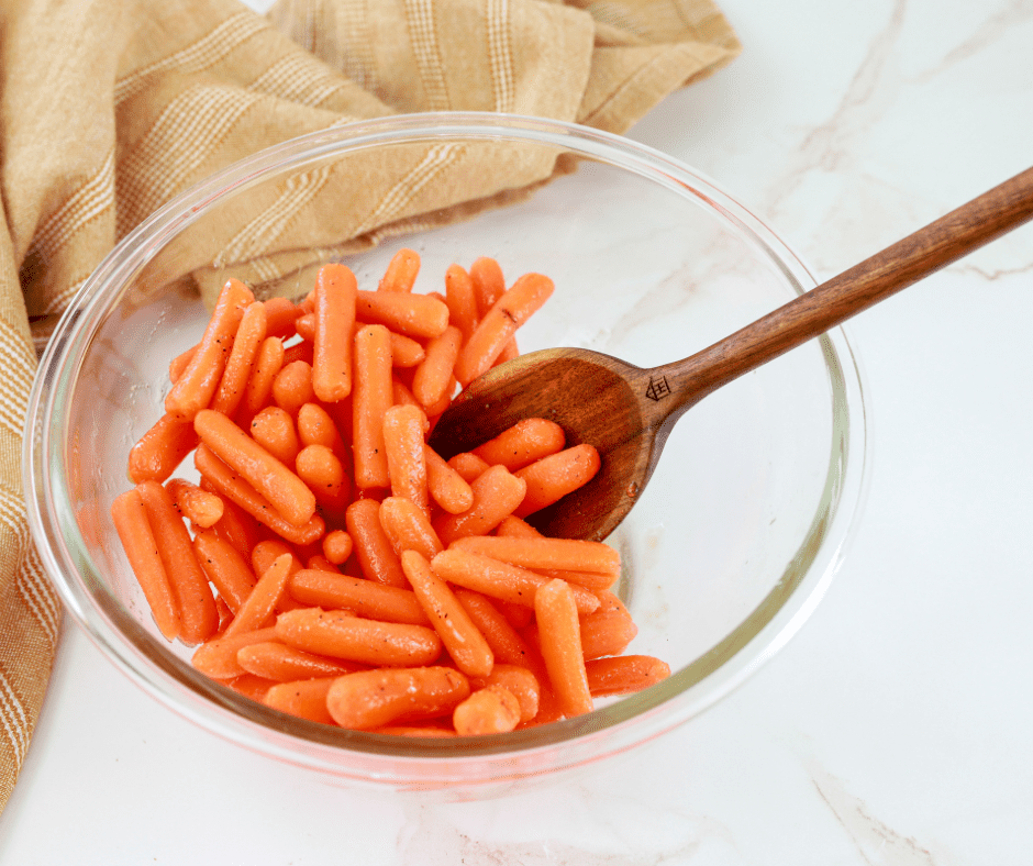 Carrots mixed with oil, honey, and seasonings in a bowl with a wooden spoon