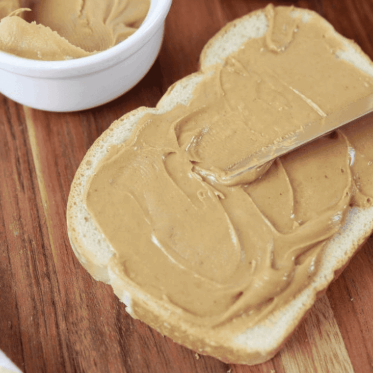 Slice of bread with peanut butter evenly spread on top, ready for sandwich assembly.