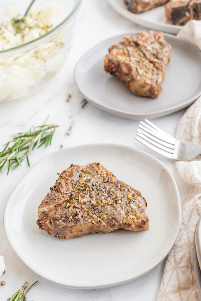 Air fryer rosemary garlic lamb chops on a plate with herbs and lemon slices