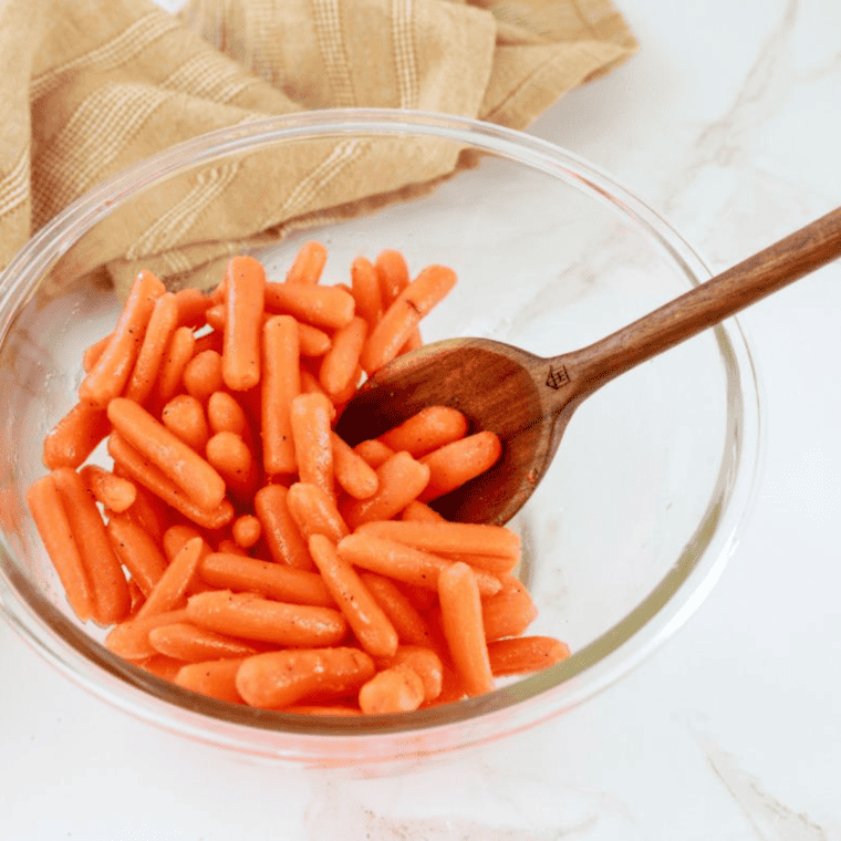 a wooden spoon mixing a glass bowl full of honey glazed carrots for air fryer