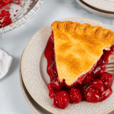 Slice of air fryer cherry pie on a white plate with a scoop of vanilla ice cream
