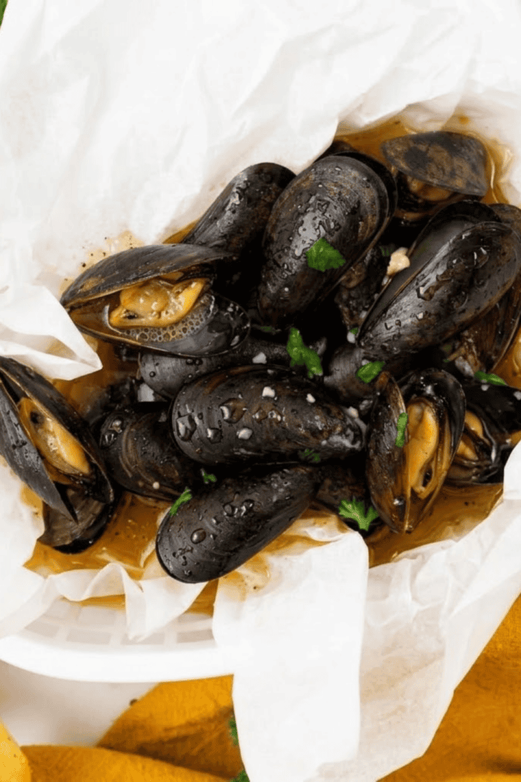 Air fryer mussels in a bowl, garnished with herbs and garlic butter, ready to serve.