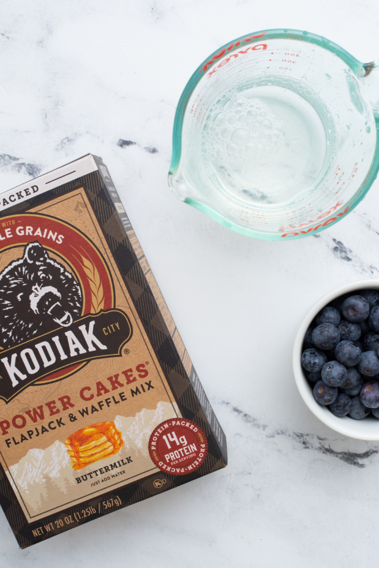 Ingredients needed for Air Fryer Pancakes from Scratch (Plus an Easy Pancake Mix Version!) on kitchen table, features pancake mix water and blueberries.