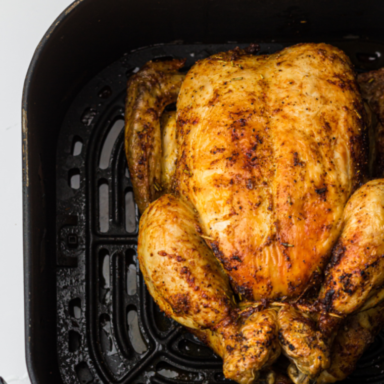 A perfectly cooked Air Fryer Whole Chicken, golden and crispy, garnished with fresh thyme and lemon slices, displayed on a serving platter.