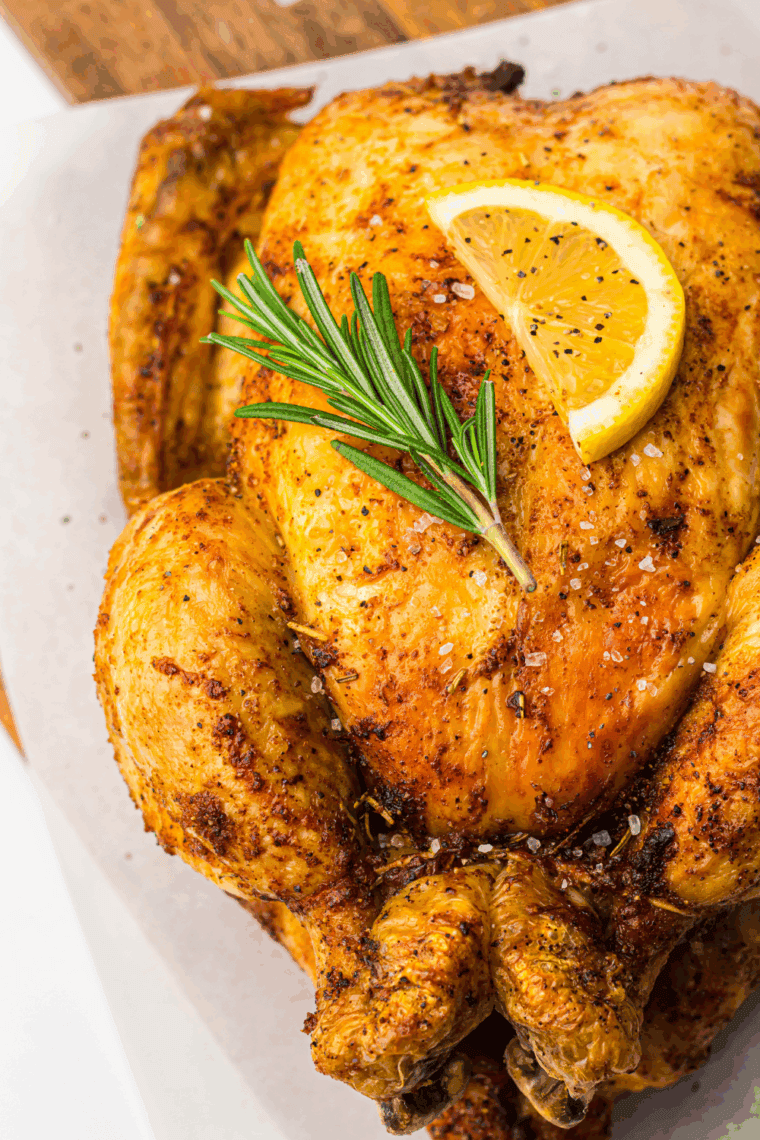 Golden-brown roasted Amish whole chicken on a serving platter, garnished with fresh herbs.