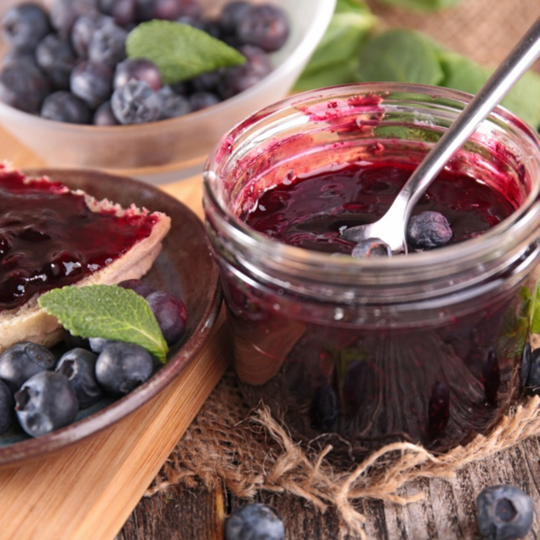 Homemade Instant Pot Blueberry Jam in a glass jar with fresh blueberries scattered around.