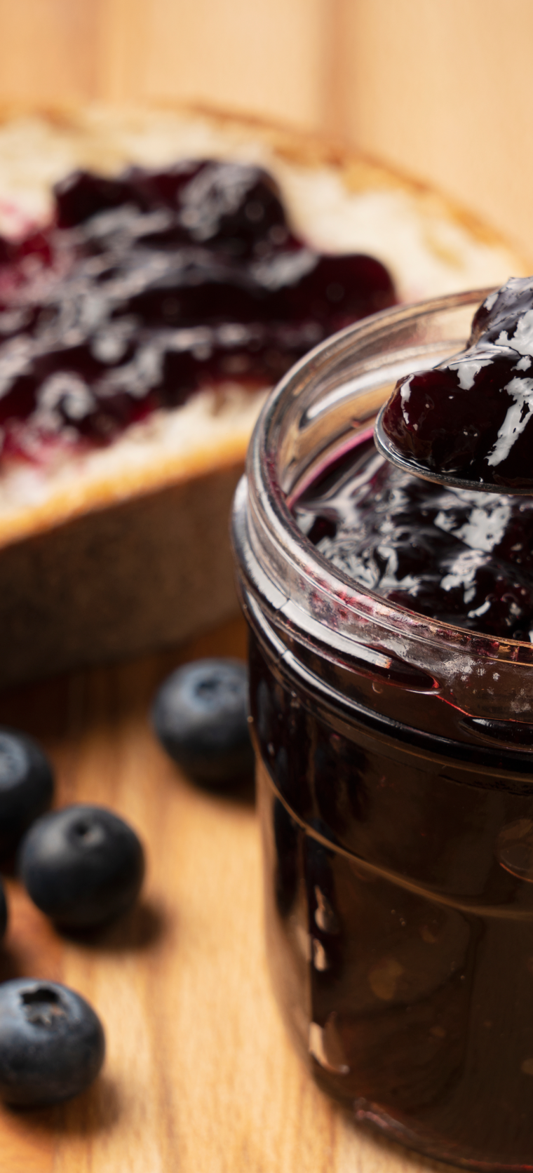 Jar of homemade Instant Pot Blueberry Jam with a spoon, surrounded by fresh blueberries on a rustic wooden table.