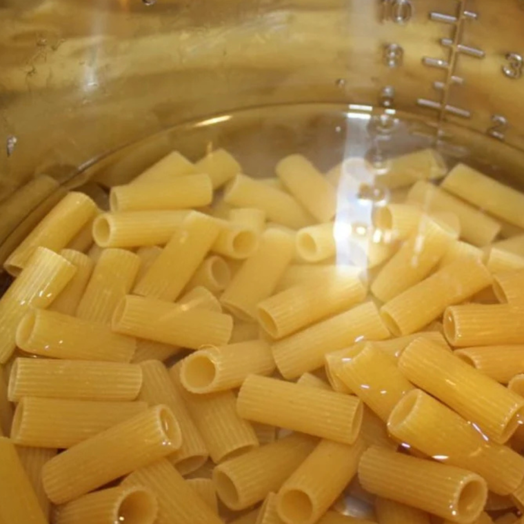 An image of penne pasta and broth being poured into the pot, capturing the layering of ingredients.