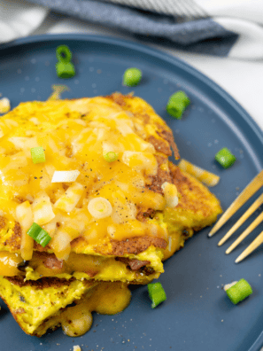 Fluffy air fryer cheese omelette folded and filled with melted cheese, served on a plate with fresh herbs.