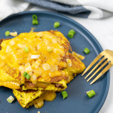 Fluffy air fryer cheese omelette folded and filled with melted cheese, served on a plate with fresh herbs.