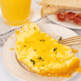Fluffy air fryer cheese omelette folded and filled with melted cheese, served on a plate with fresh herbs.