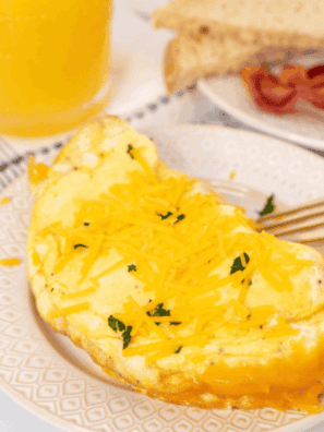 Fluffy air fryer cheese omelette folded and filled with melted cheese, served on a plate with fresh herbs.