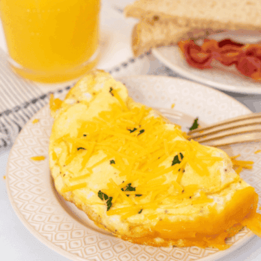 Fluffy air fryer cheese omelette folded and filled with melted cheese, served on a plate with fresh herbs.