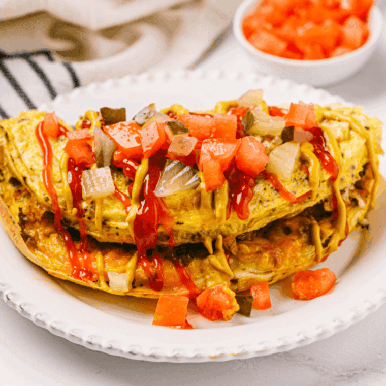 Fluffy air fryer cheese omelette folded in half on a plate, filled with melted cheese and topped with fresh herbs.