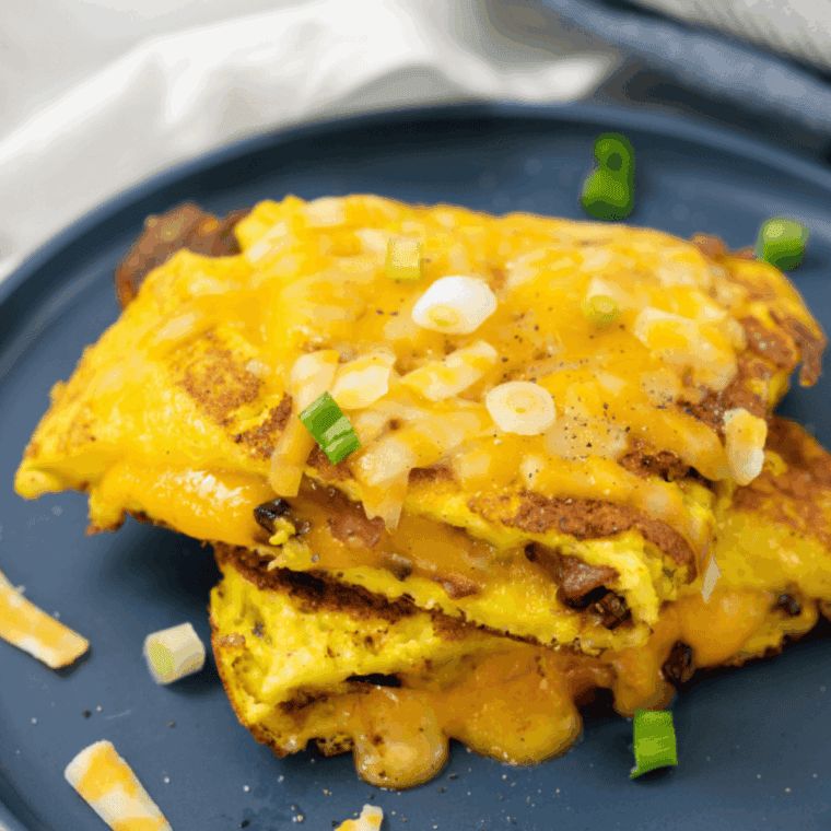 Golden, fluffy air fryer cheese omelette filled with melted cheddar and served on a white plate with herbs.