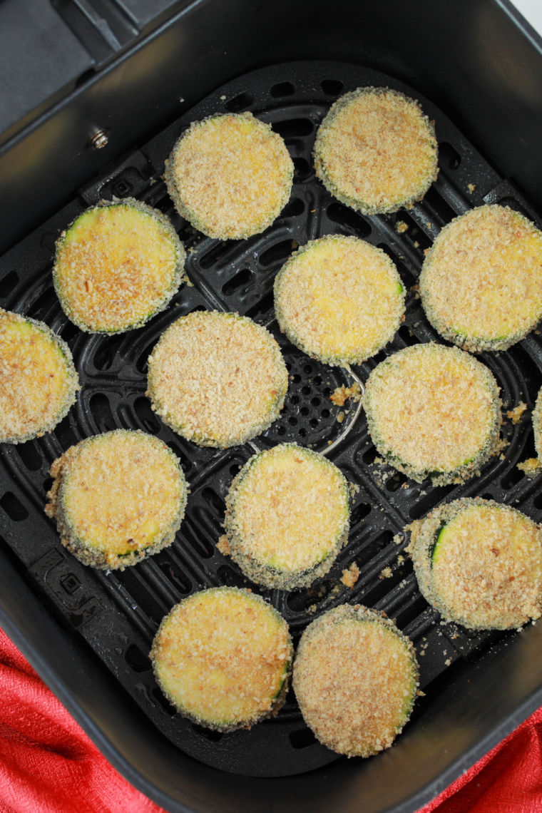 Arranging breaded zucchini in air fryer basket and lightly spraying with oil