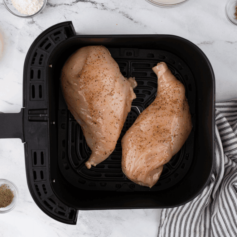 Seasoned chicken breasts cooking in an air fryer basket in a single layer.