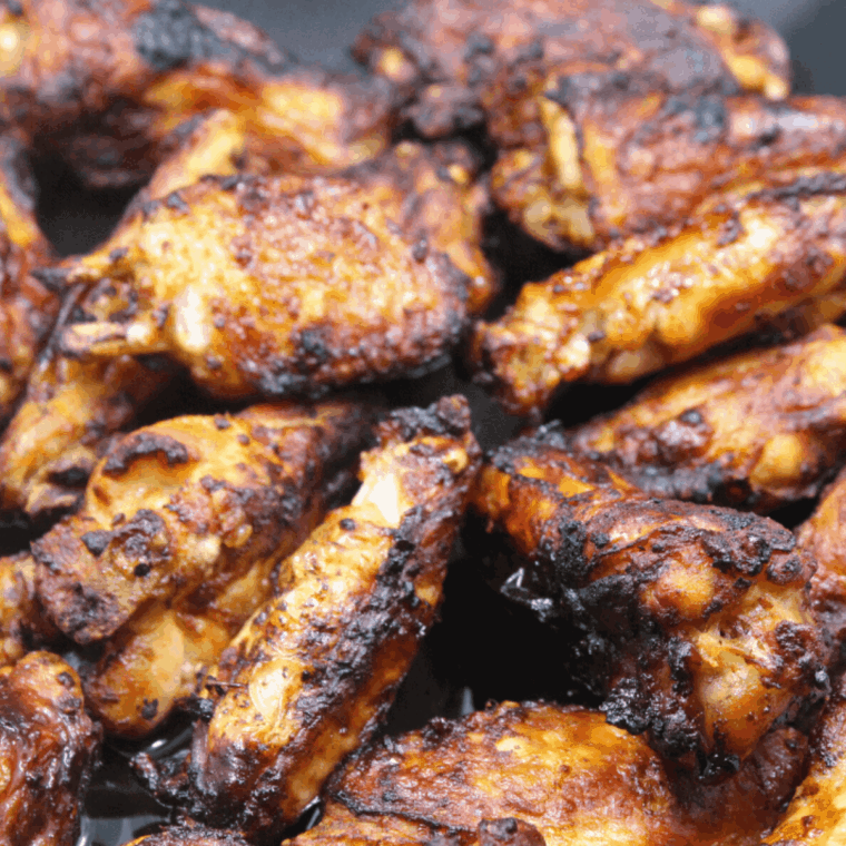 Golden-brown air fryer chicken wings coated in a lemon dijon sauce, garnished with fresh herbs on a white plate.