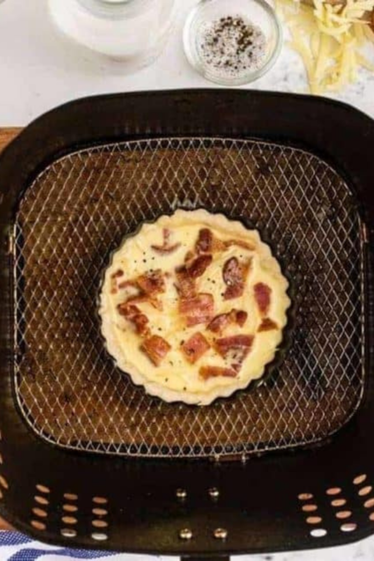 Air Fryer Bacon and Egg Quiche Lorraine with golden crust, fluffy eggs, melted Swiss cheese, and crispy bacon, served in a round baking dish.