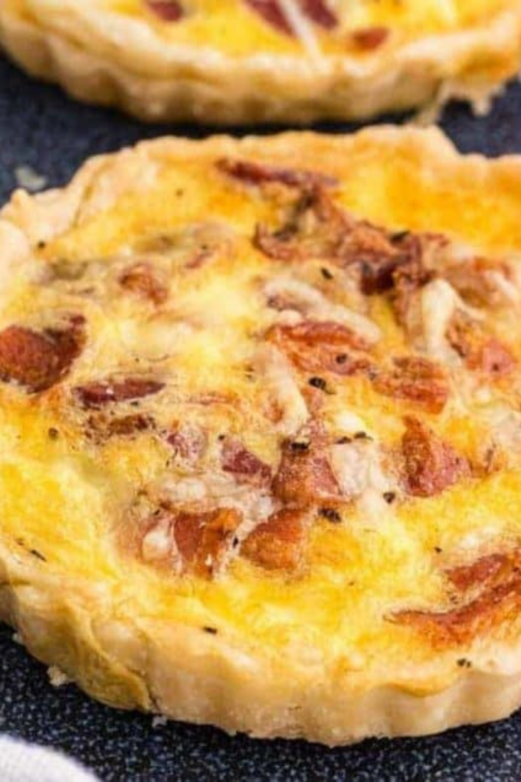 Air Fryer Bacon and Egg Quiche Lorraine with golden crust, fluffy eggs, melted Swiss cheese, and crispy bacon, served in a round baking dish.