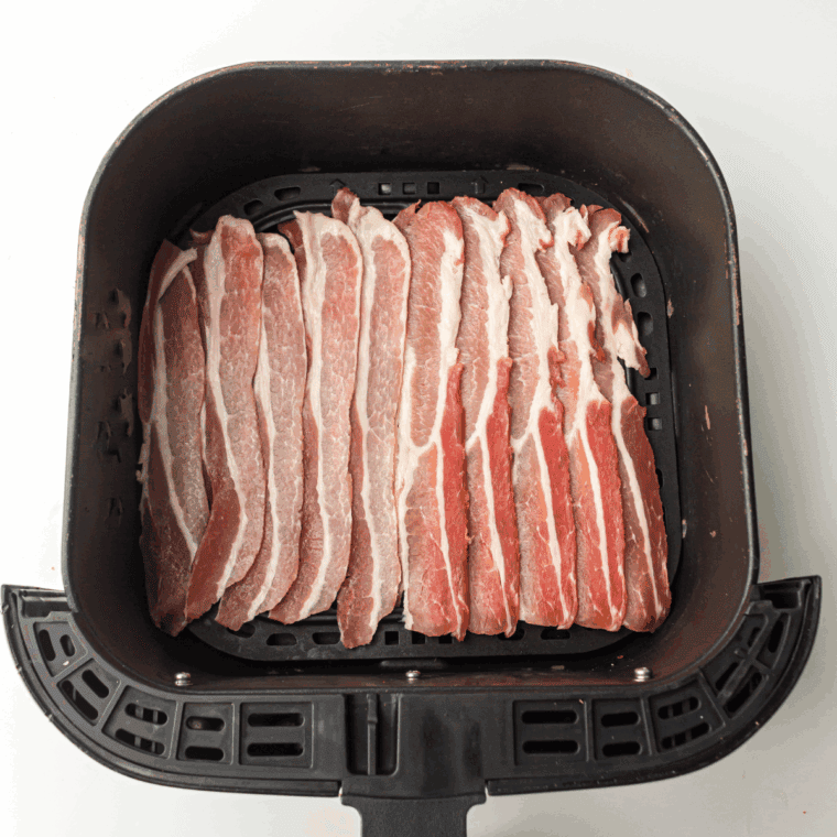 Raw bacon in the air fryer basket.