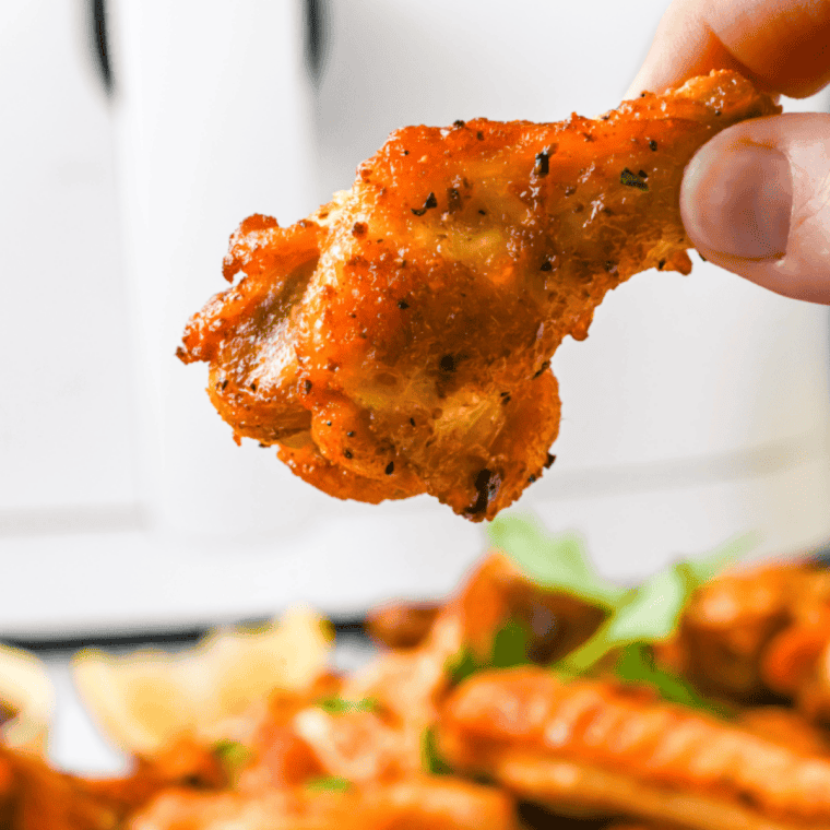 Air fryer cooked chicken wings with browned crispy skin served with sauce for dipping.