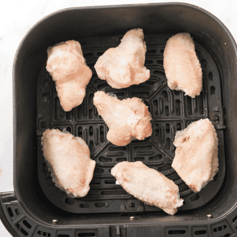 Frozen chicken wings placed in an air fryer basket in a single layer with space between pieces, no oil or seasoning added yet.
