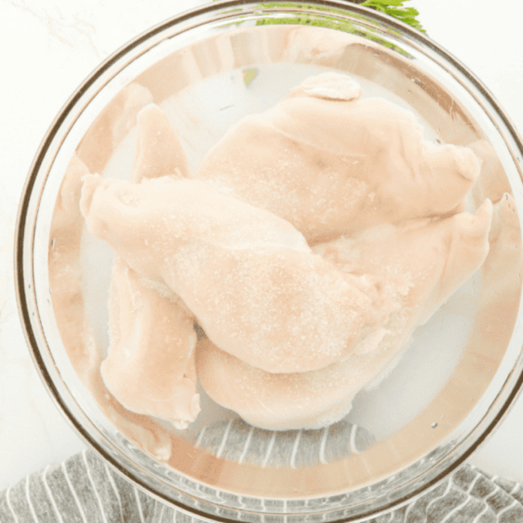 Raw chicken breasts being seasoned with herbs and spices in a mixing bowl.