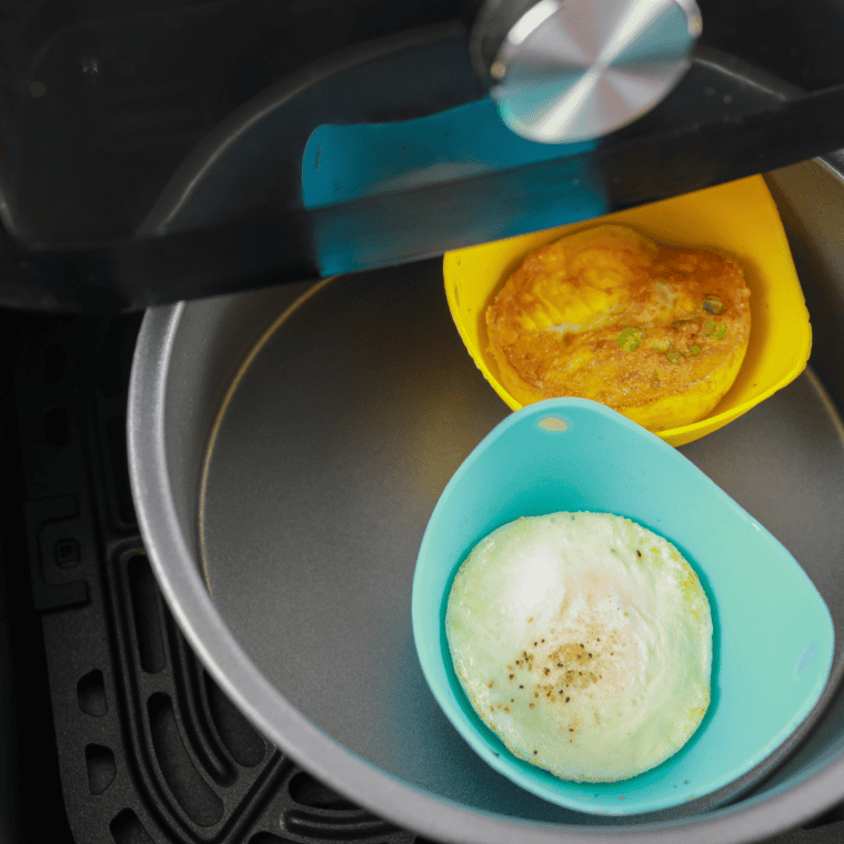 Cracking an egg into a greased ramekin to make an air fryer bagel breakfast sandwich