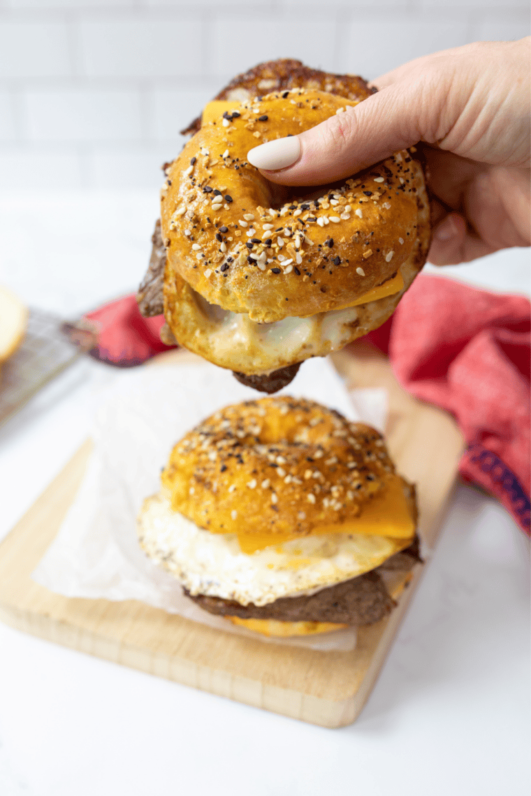 Assembling an air fryer bagel breakfast sandwich with cheese, baked egg, and sausage on a homemade bagel