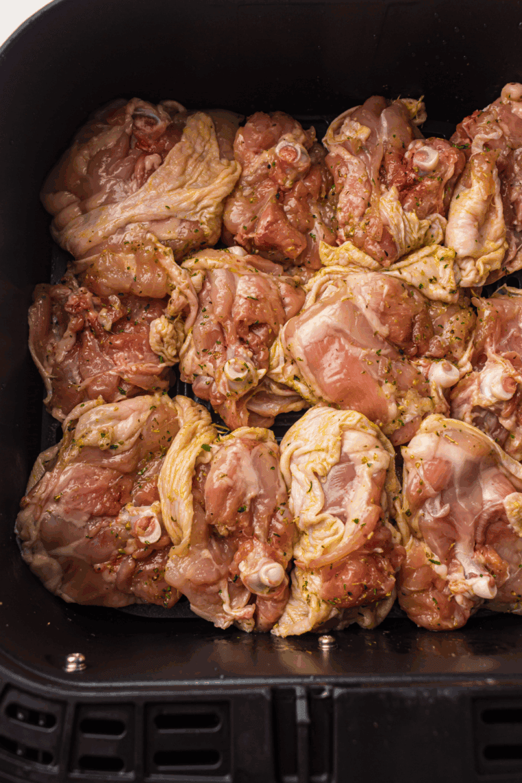 Coated chicken thighs arranged in a single layer in the air fryer basket, cooking at 360&deg;F and flipped halfway for even browning.