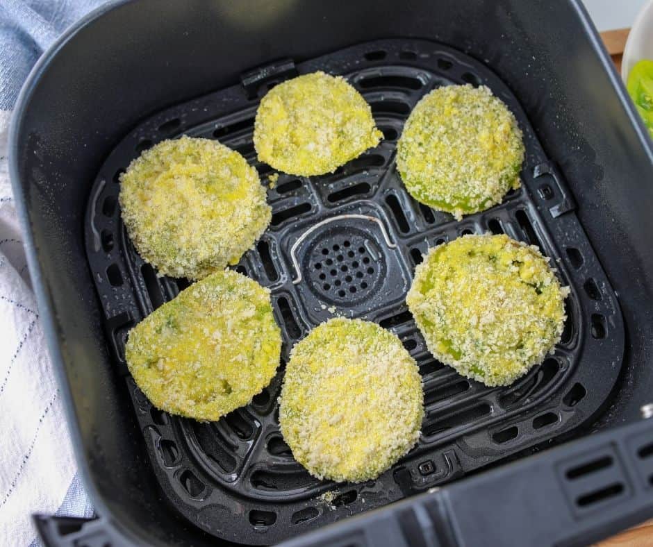 Top view of square Air Fryer basket with six uncooked breaded green tomatoes in it. 